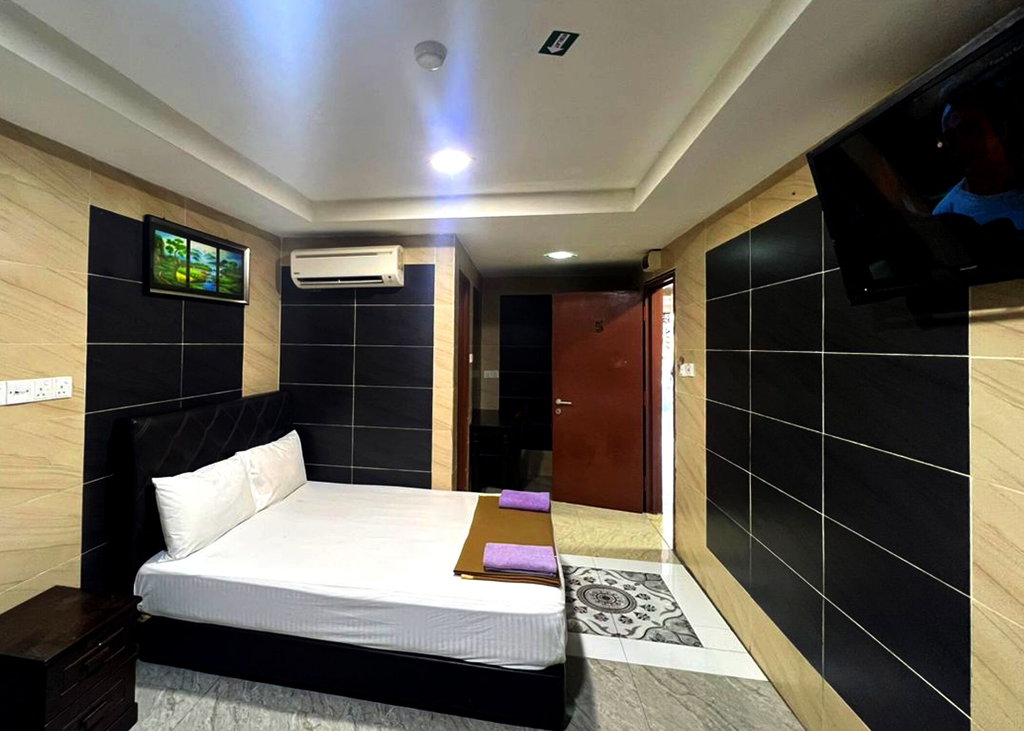 Una habitación de hotel moderna con una cama grande, un televisor de pantalla plana montado en la pared y un equipo de aire acondicionado.