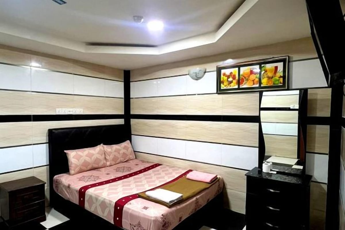 A bedroom with a bed, a bedside table, a mirror, and a wall-mounted picture of fruits.