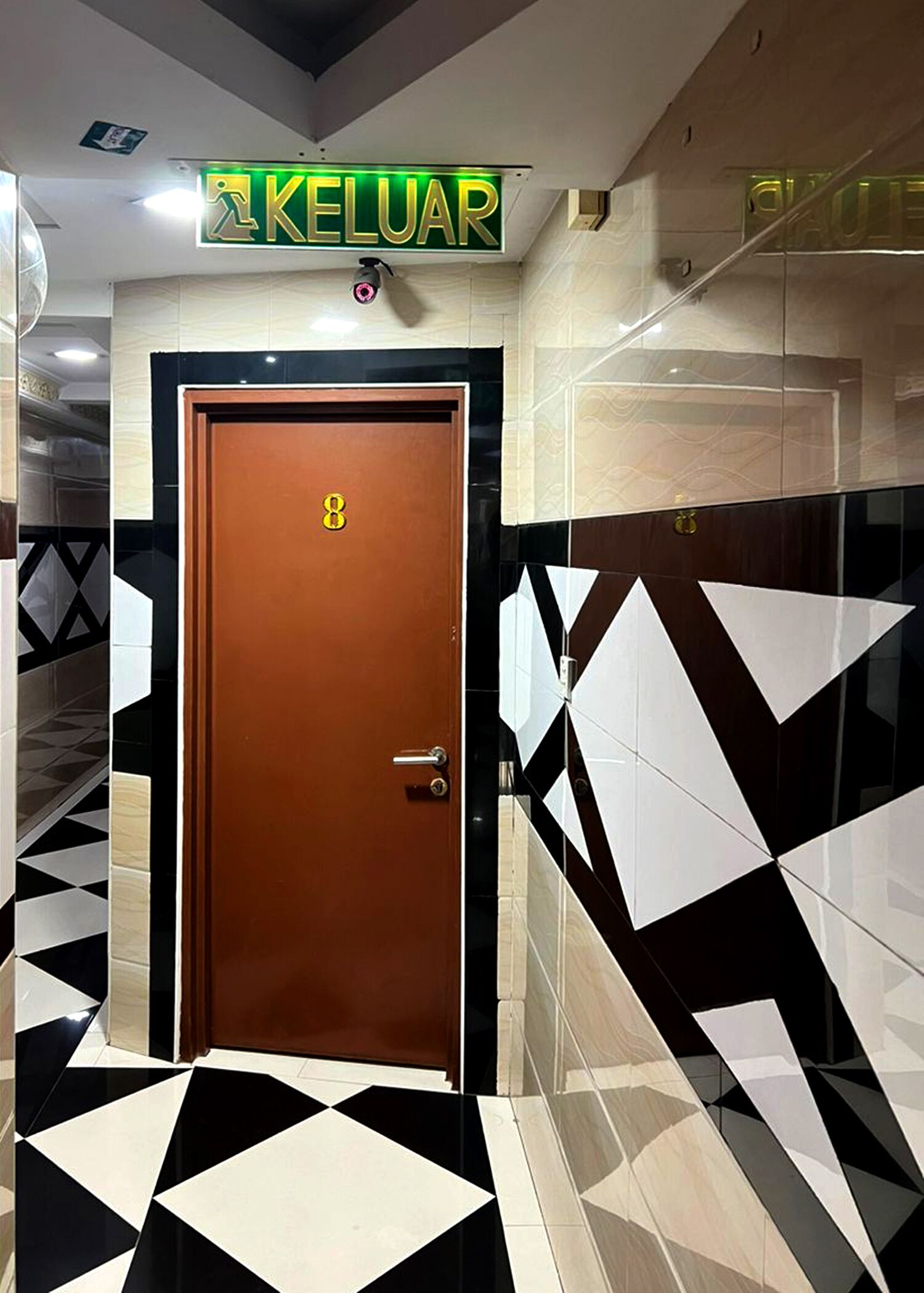 A hallway with a brown door marked with the number 8, leading to a room. The floor has a black and white geometric pattern.