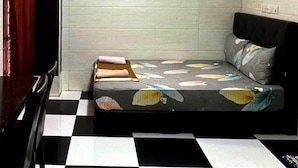 Une pièce avec un sol à carreaux, un lit recouvert d’une couvre-lit à motifs floraux, une lampe fixée au mur et un tableau encadré.