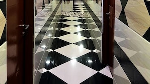 Un couloir doté d’un sol à carreaux, d’un plafond orné et de portes numérotées 15 et 18.
