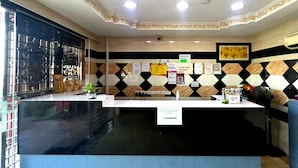 Un espace d’accueil comprenant un comptoir d’enregistrement, une grande fenêtre avec des stores et un mur décoré de carreaux hexagonaux et de divers panneaux.