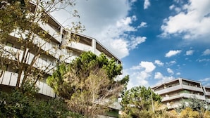 Um edifício residencial de vários andares com varandas, rodeado por vegetação densa.