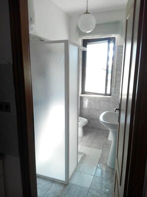 Un pasillo estrecho que conduce a un baño con ventana, lavamanos e inodoro.