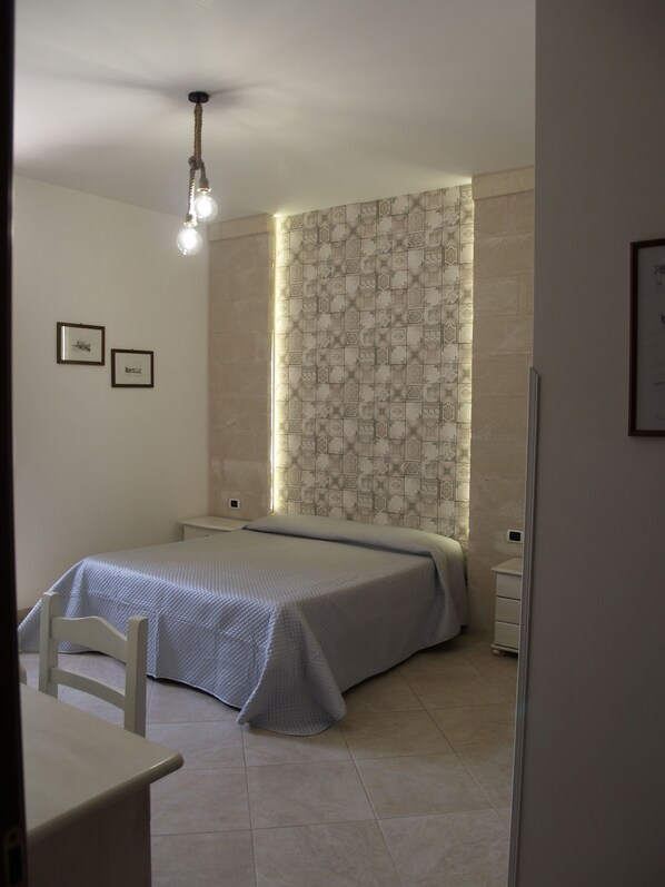 A bedroom with a bed, a desk, and a chair. There are two framed pictures on the wall. - Masseria Don Sante (Fasano)