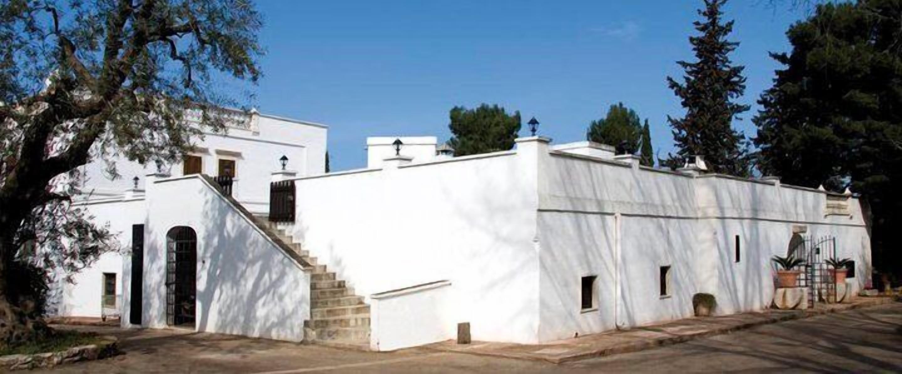 A white building with a staircase leading to an entrance, surrounded by trees.