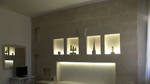 Une chambre d’hôtel avec un grand lit, une table de chevet, un petit bureau avec un ordinateur et une étagère murale agrémentée d’objets décoratifs.