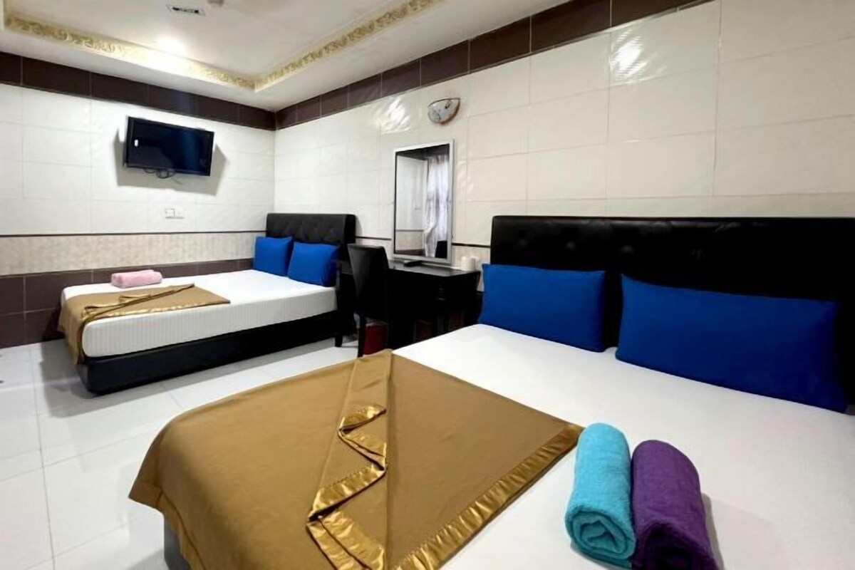 Ett hotellrum med två sängar, ett skrivbord, en tv och en väckarklocka på väggen.