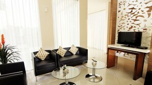 Una sala de estar moderna con un sofá negro, dos mesas de centro de vidrio, un televisor sobre un mueble de madera y un panel decorativo en la pared.