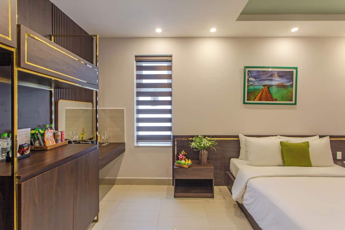 Una habitación de hotel con una cama, una mesita de noche con un jarrón, una ventana con persianas y un cuadro en la pared.