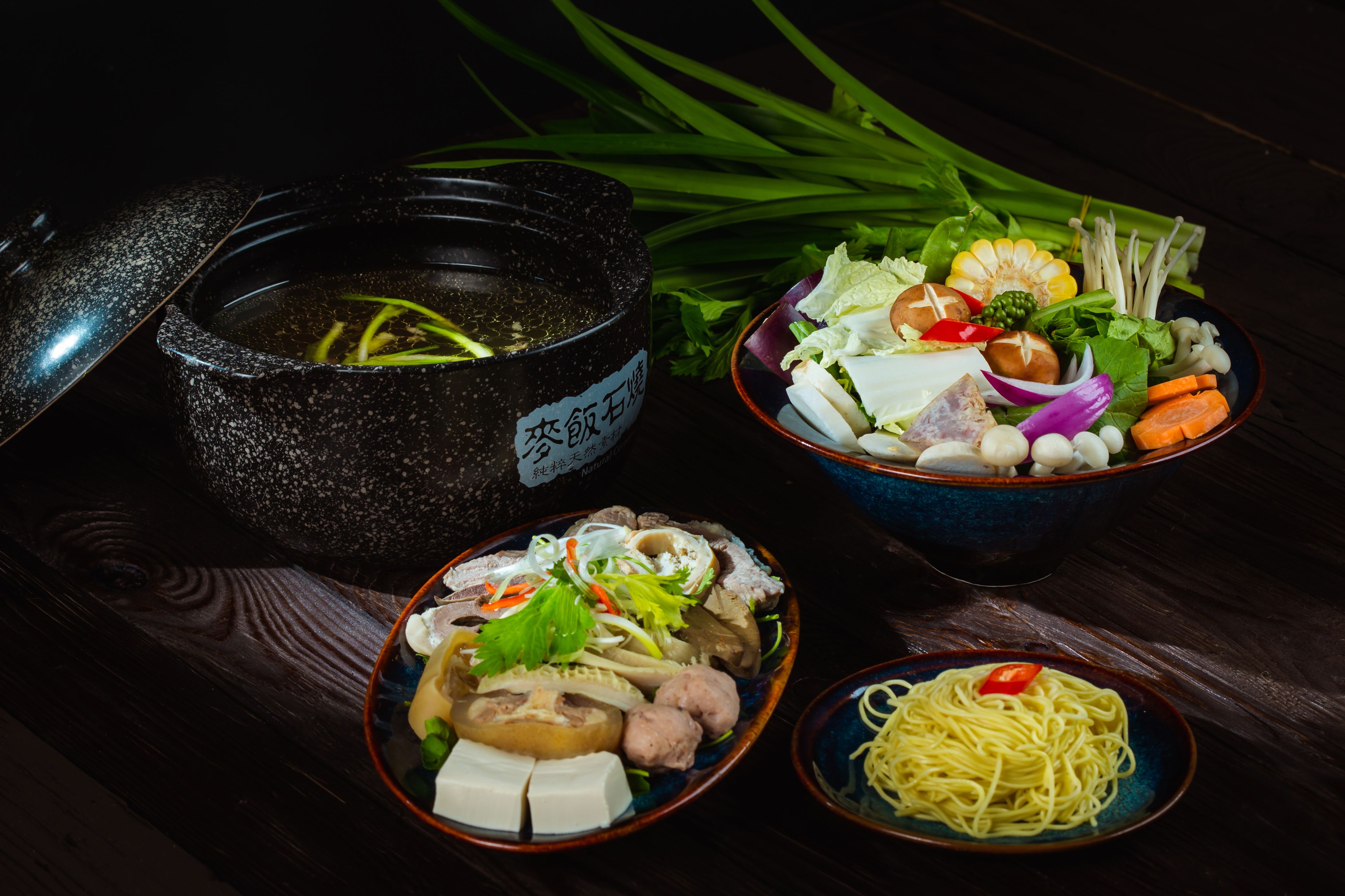 A table with various dishes including a bowl of soup, a plate of noodles, and a bowl of salad with vegetables and meat.