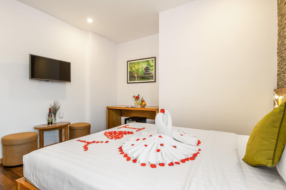 Habitación de hotel con una cama bien hecha, un televisor de pantalla plana montado en la pared, un escritorio con un jarrón de flores y un cuadro en la pared.