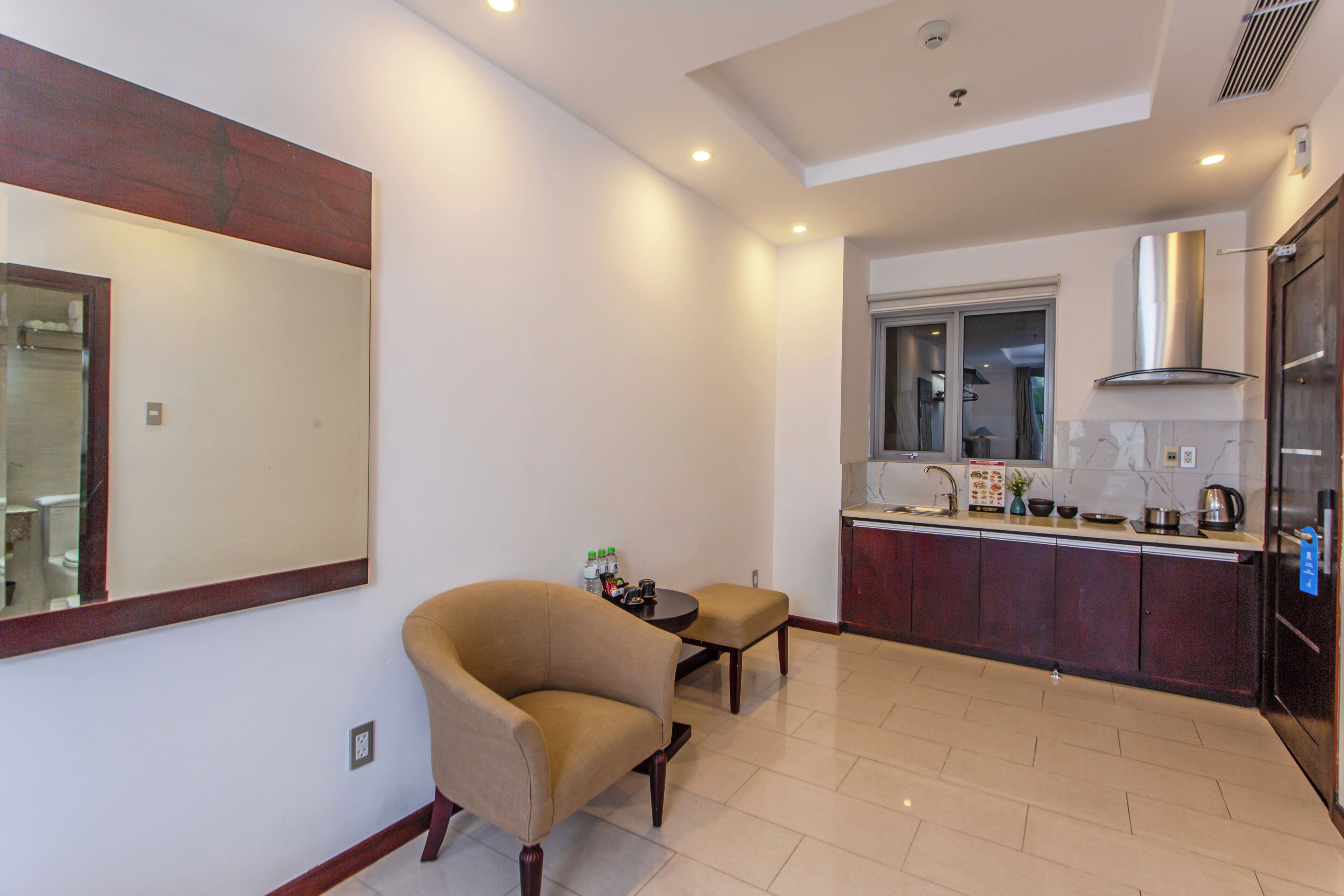 A modern kitchen with a large mirror, a dining area with a chair and table, and a view into the adjacent bathroom.