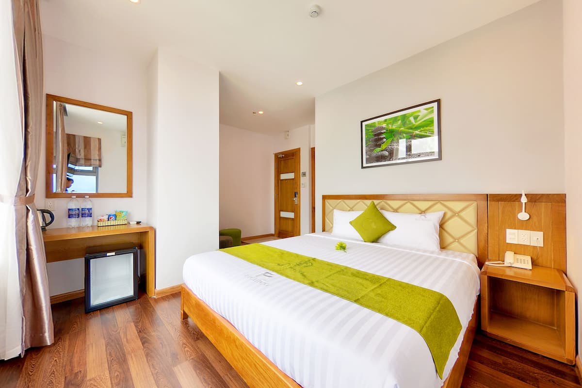 Habitación de hotel con cama, mesita de noche, un escritorio pequeño con espejo, refrigerador y un cuadro en la pared.
