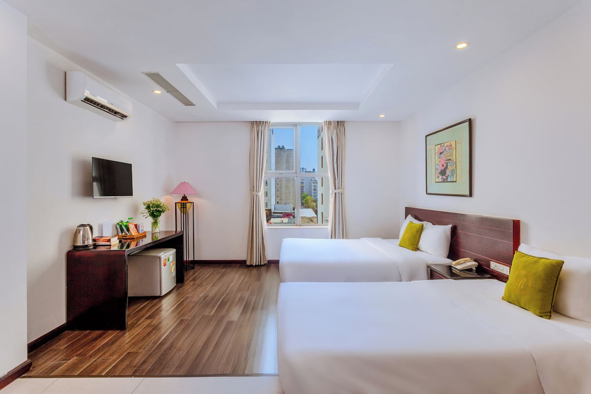 Habitación de hotel con dos camas, un escritorio con lámpara, televisor y ventana con cortinas.