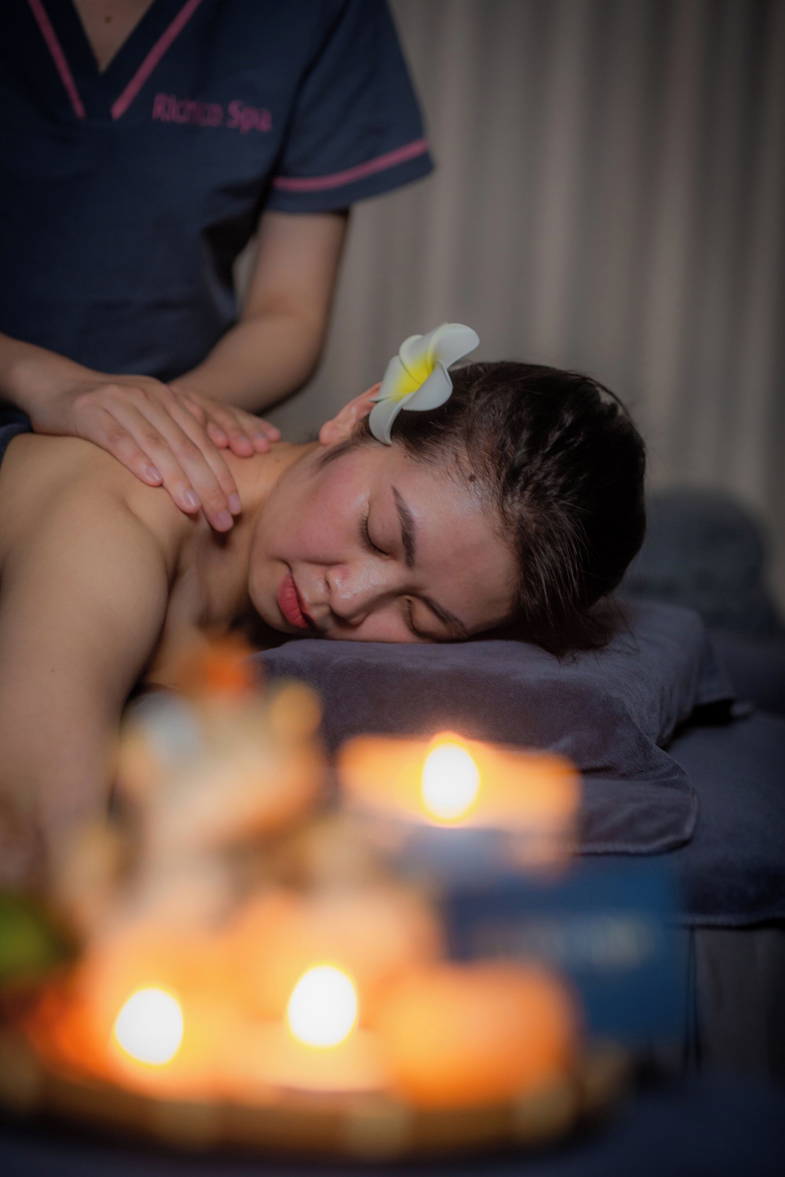 Sesión de terapia de masaje con una persona acostada en una camilla, manos de terapeuta en su espalda y velas al frente.