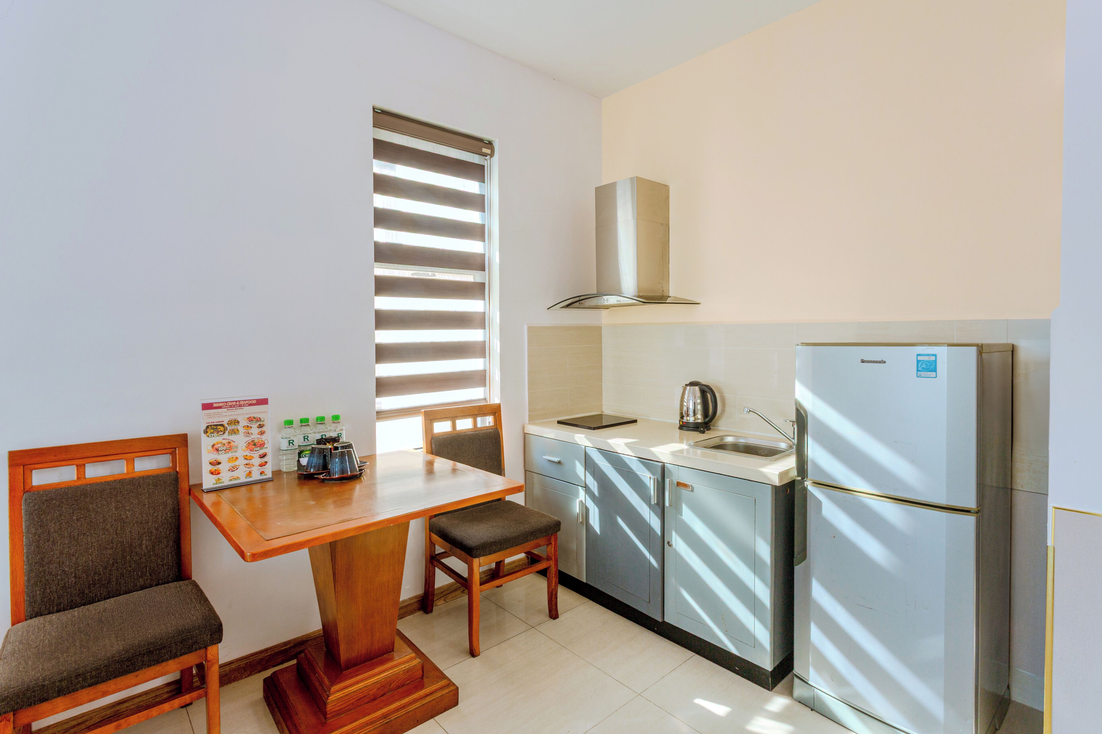A compact kitchen with a dining table, chairs, a refrigerator, and a window with blinds.
