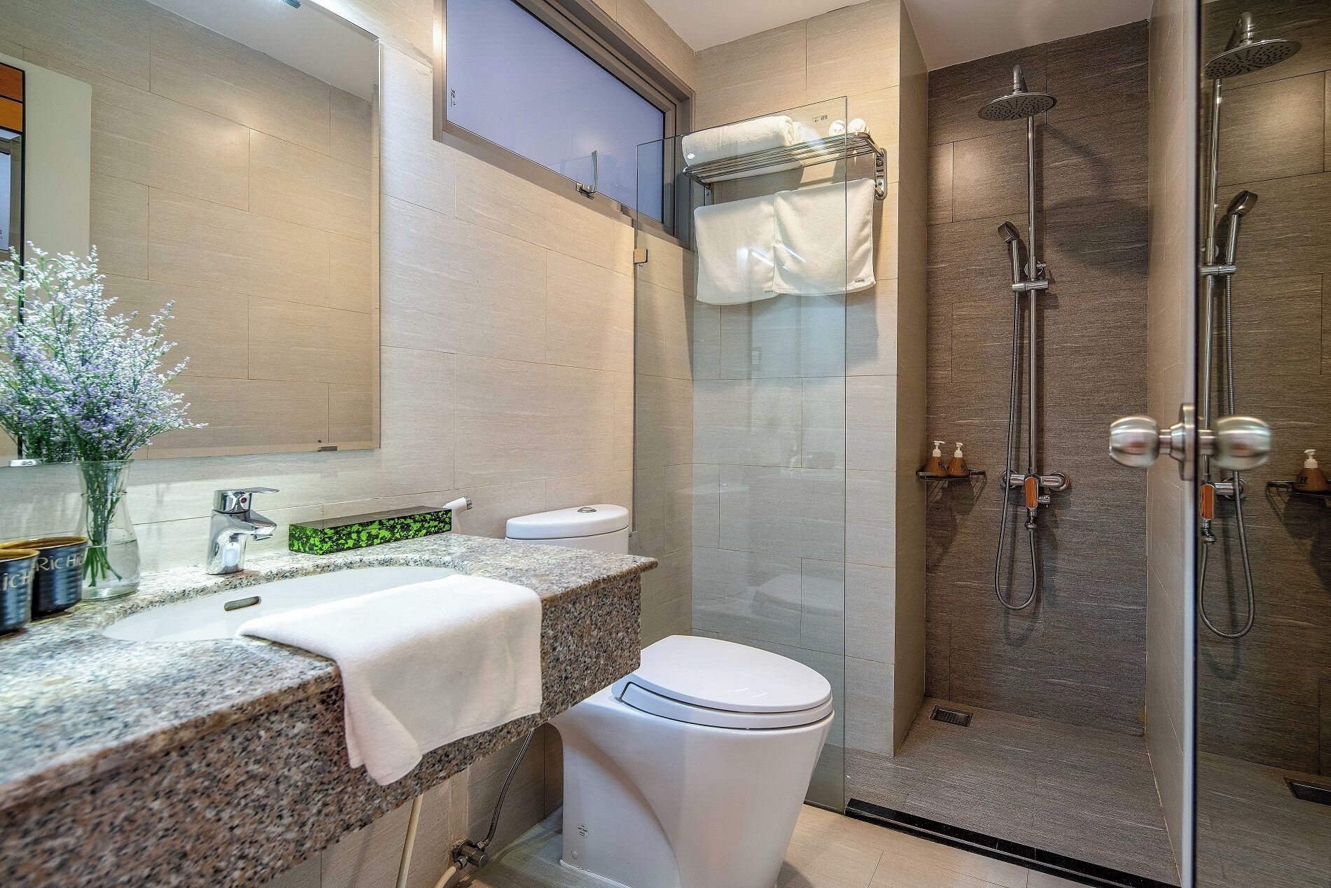 Un baño moderno con encimera de granito, inodoro blanco, cabina de ducha con mampara de cristal y espejo sobre el lavabo.