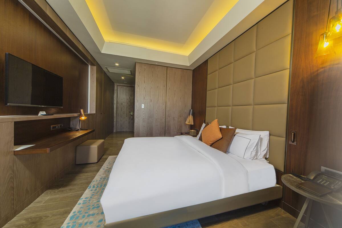 A modern hotel room with a large bed, a flat-screen TV, a bedside table, and a desk area.