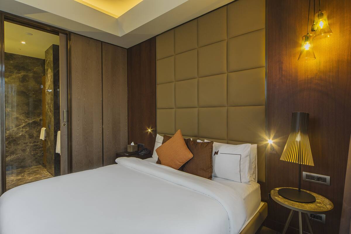 A modern hotel room with a large bed, a bedside table, a lamp, and a mirror.