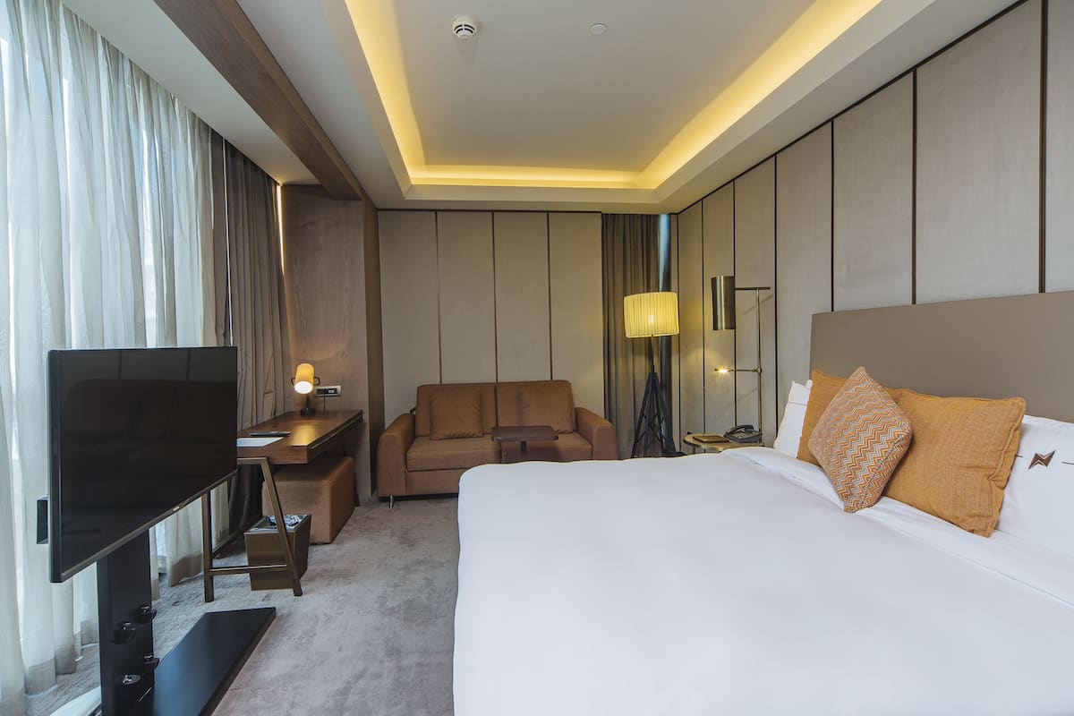 A hotel room with a large bed, a TV, a desk, and a sofa.