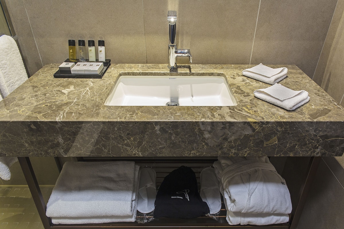 A bathroom with a marble sink, two towels, and a bottle of shampoo.