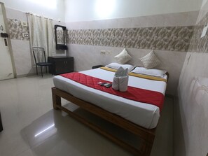 A hotel room with a bed, a wooden bench, a chair, a small table, and a mirror on the wall.