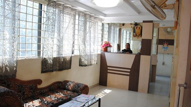 A hotel lobby with a reception desk, patterned curtains, a sofa, and a fan. - Just Guest House (Chennai)