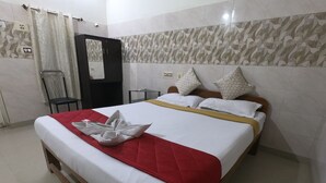 A hotel room with a bed, a red and white bedspread, a towel on the bed, a chair, a small table, and a wall with patterned tiles. - Just Guest House (Chennai)