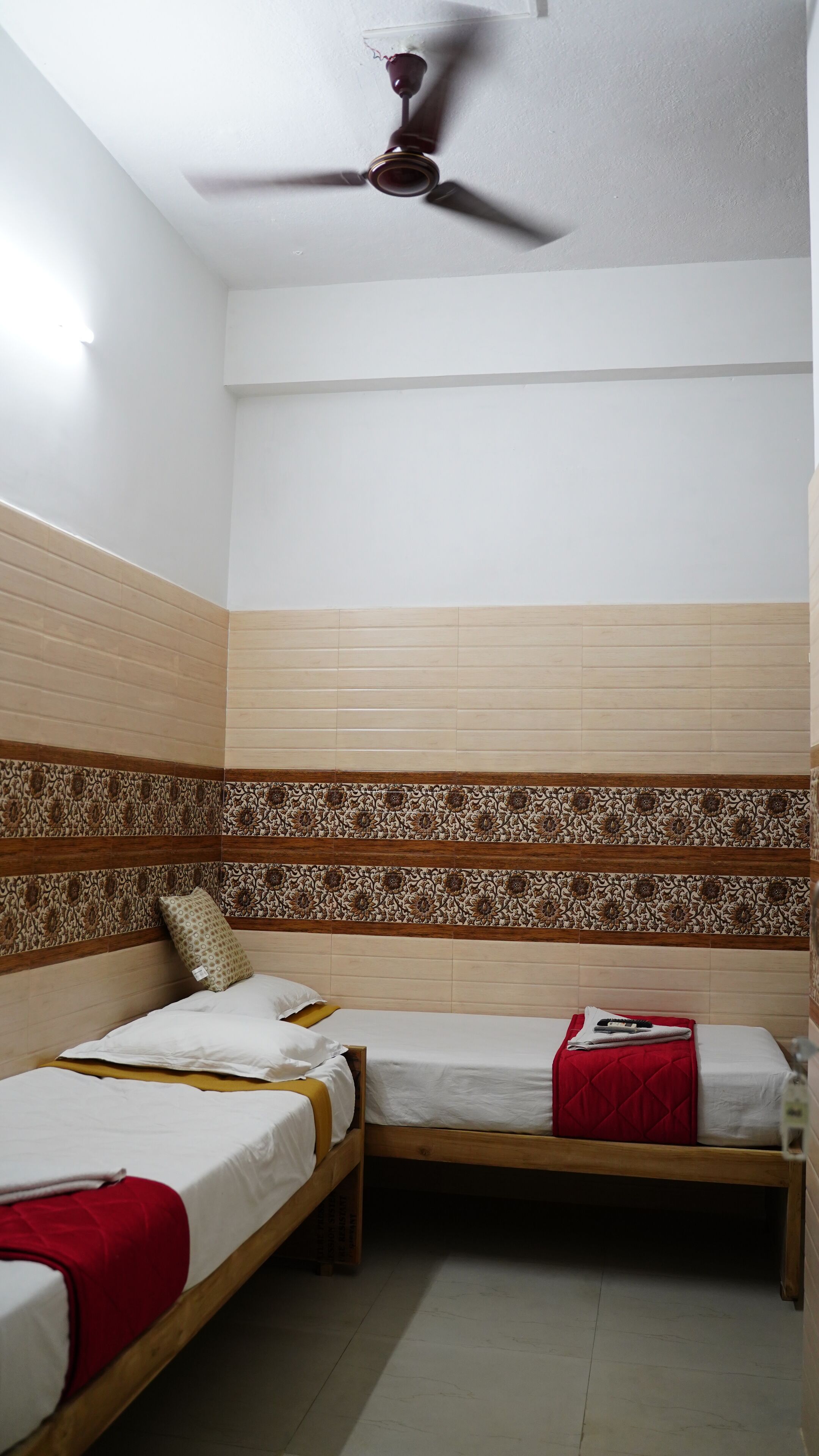 A room with two single beds, a ceiling fan, and patterned wall tiles.