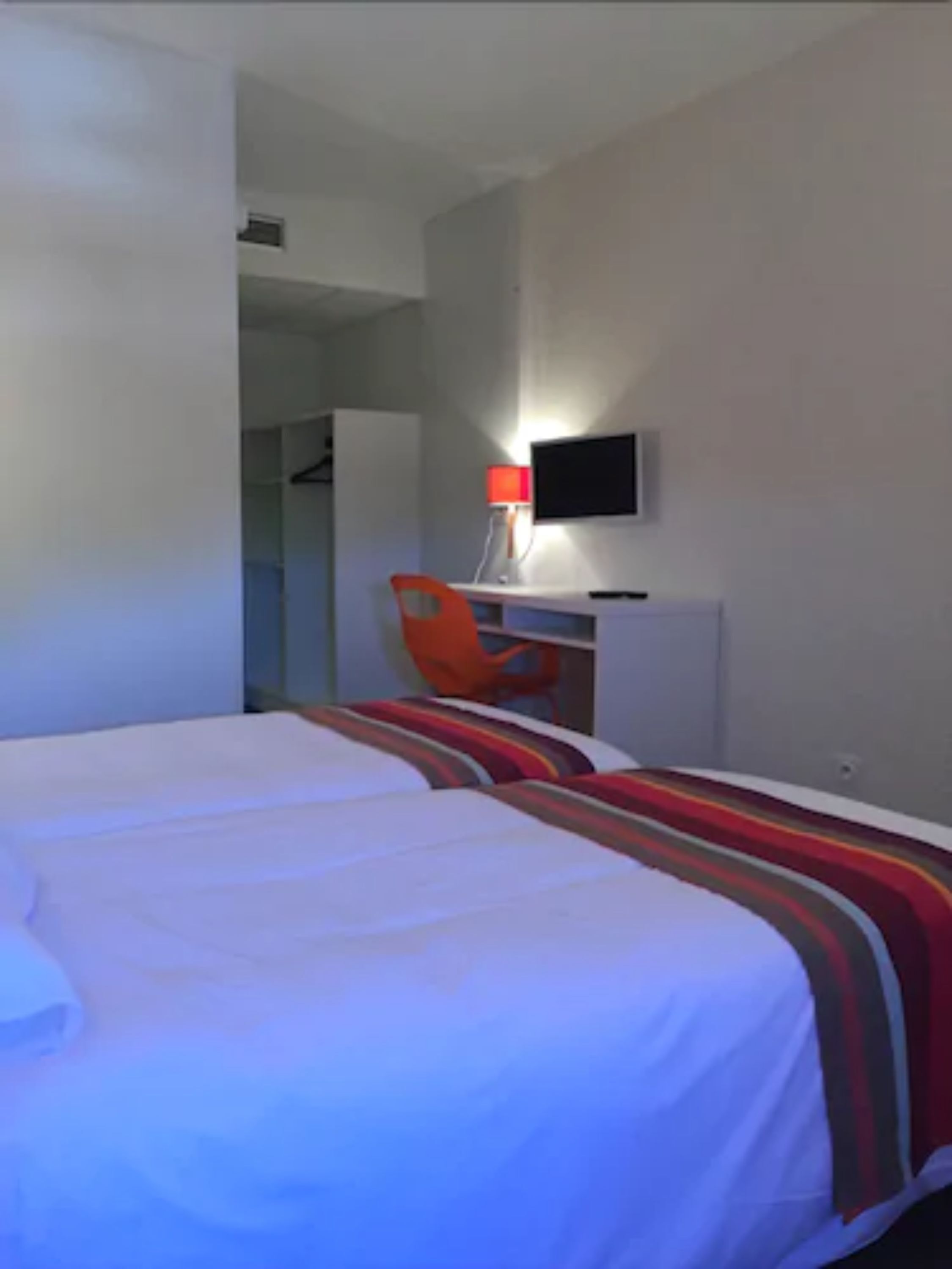 A hotel room with a bed, a desk, a chair, and a TV.