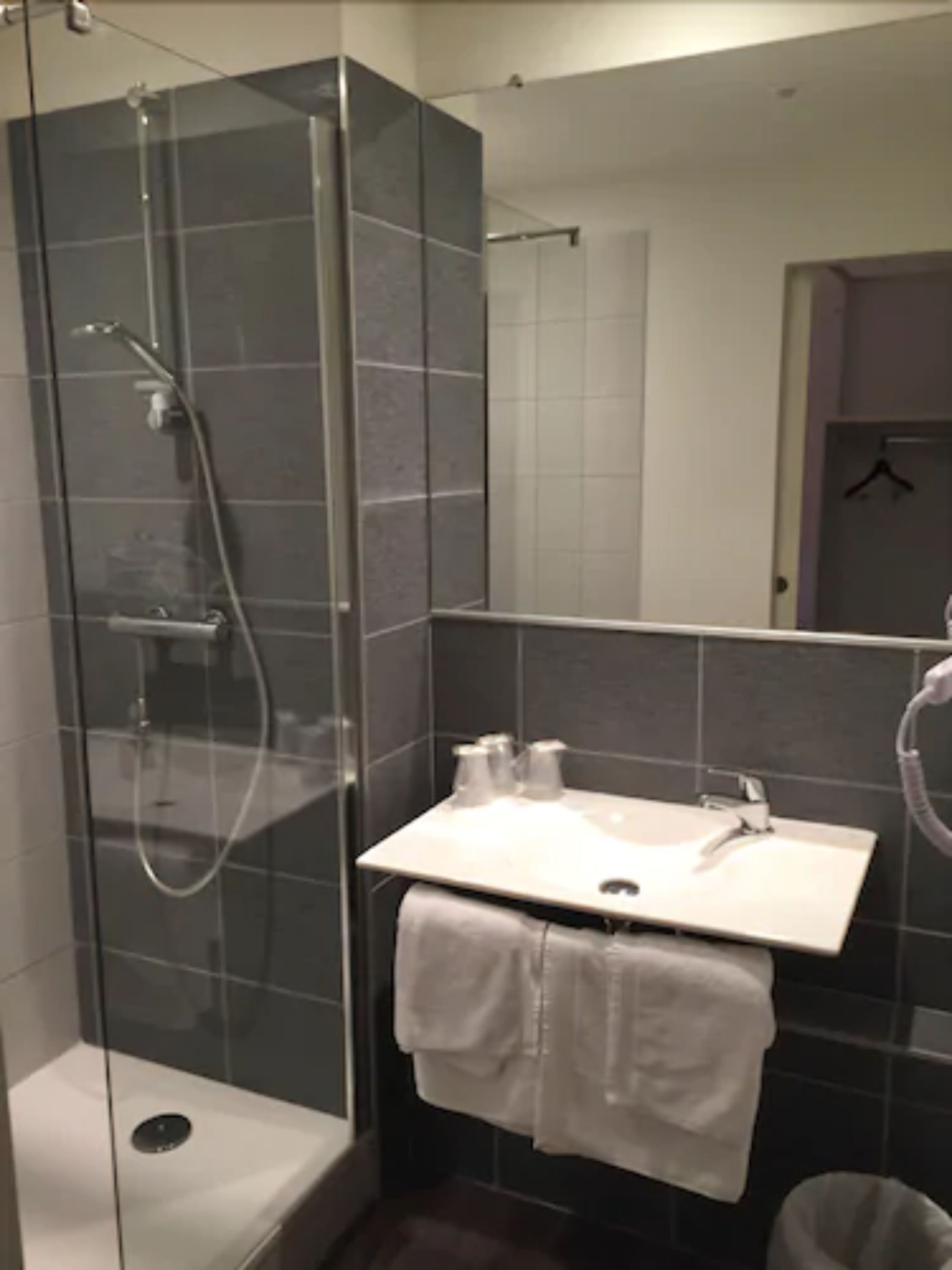 A modern bathroom with a glass-enclosed shower, a white sink, and a towel rack.