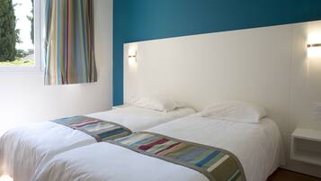 Een hotelkamer met twee bedden, een raam met gordijnen en een wandlamp.