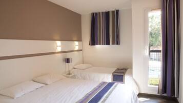 Une chambre d’hôtel avec deux lits, une table de chevet avec une lampe, une fenêtre avec des rideaux et une vue sur la verdure.
