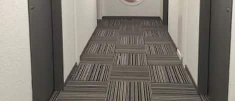 Un pasillo con alfombra estampada, puertas grises y un adorno circular en la pared.