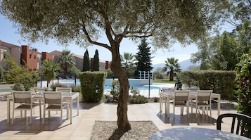 Un patio al aire libre con mesas y sillas, una piscina y follaje circundante.