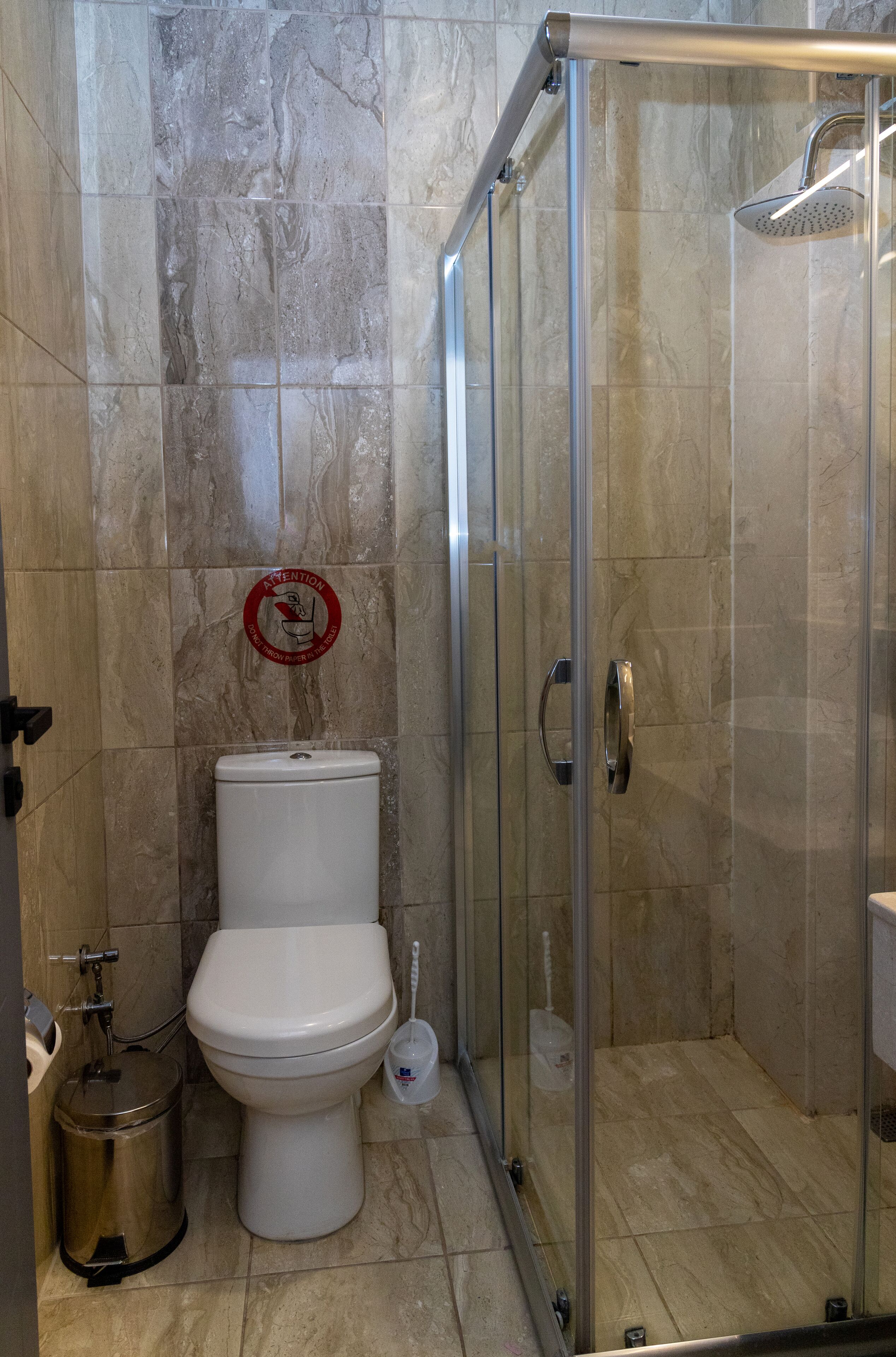 Un baño con inodoro, cabina de ducha de vidrio y cubo de basura.