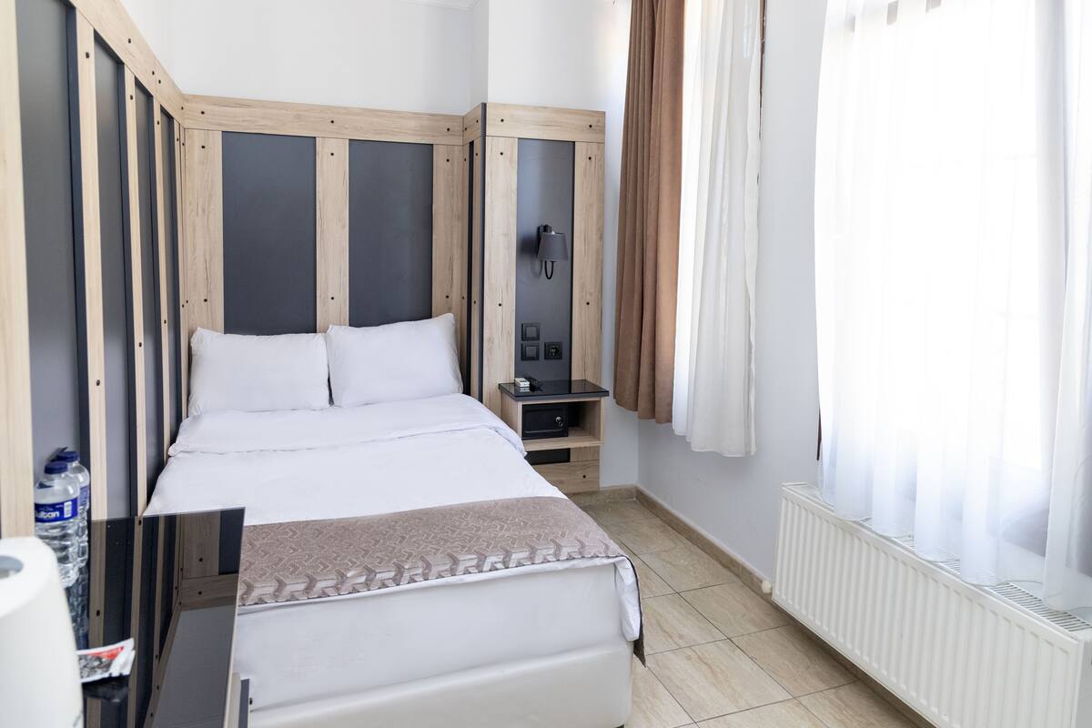 A hotel room with a bed, bedside table, lamp, and a window with curtains.