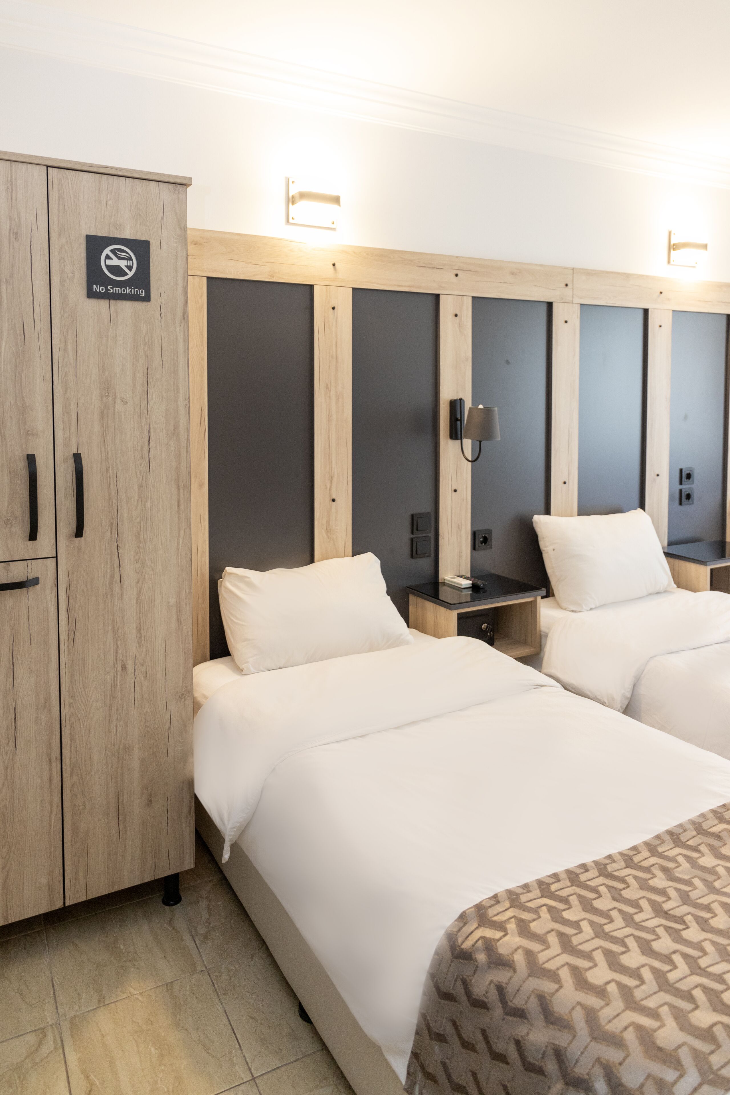 A hotel room with two beds, a wardrobe, and a 'No Smoking' sign.
