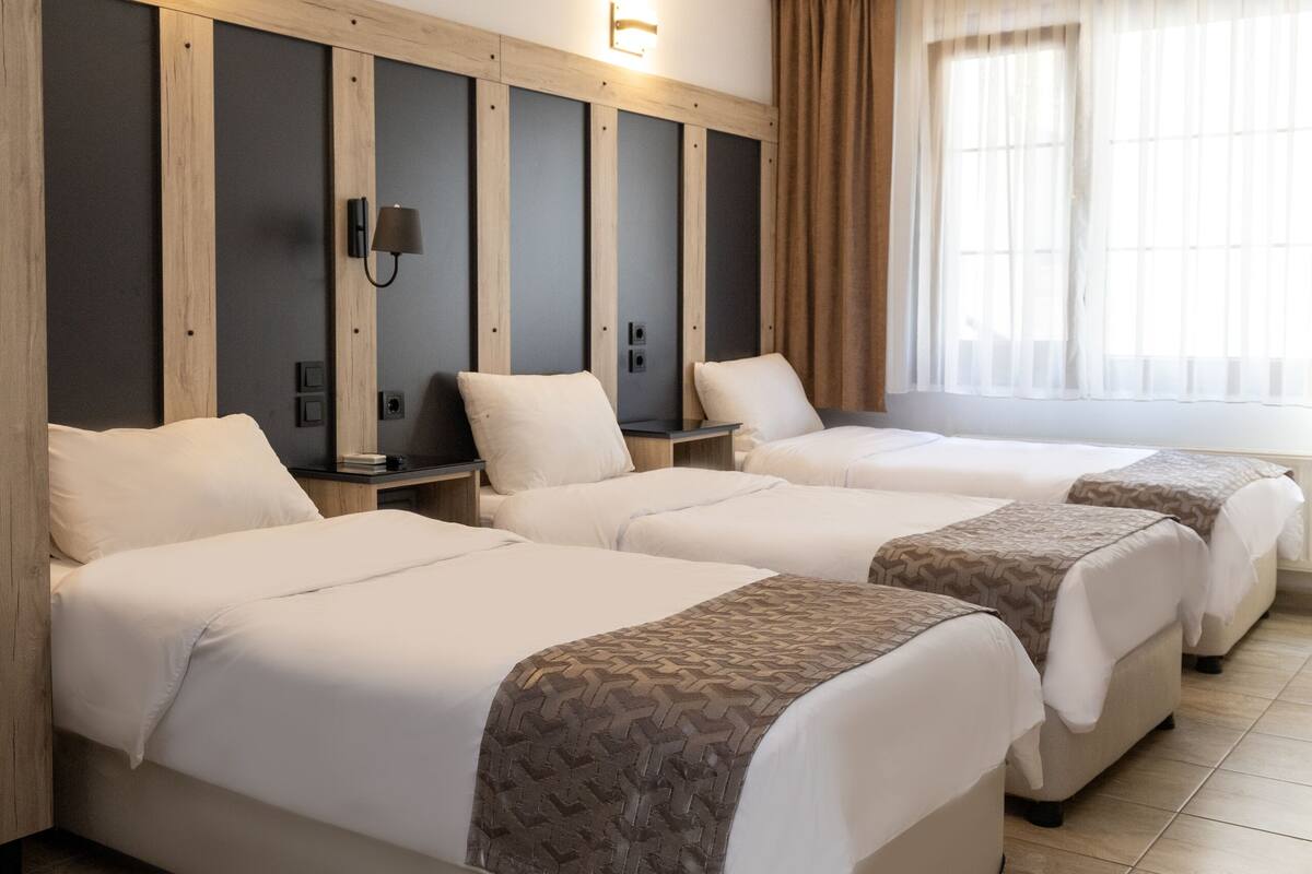A hotel room with three beds, a large window with curtains, and a wall-mounted light fixture.