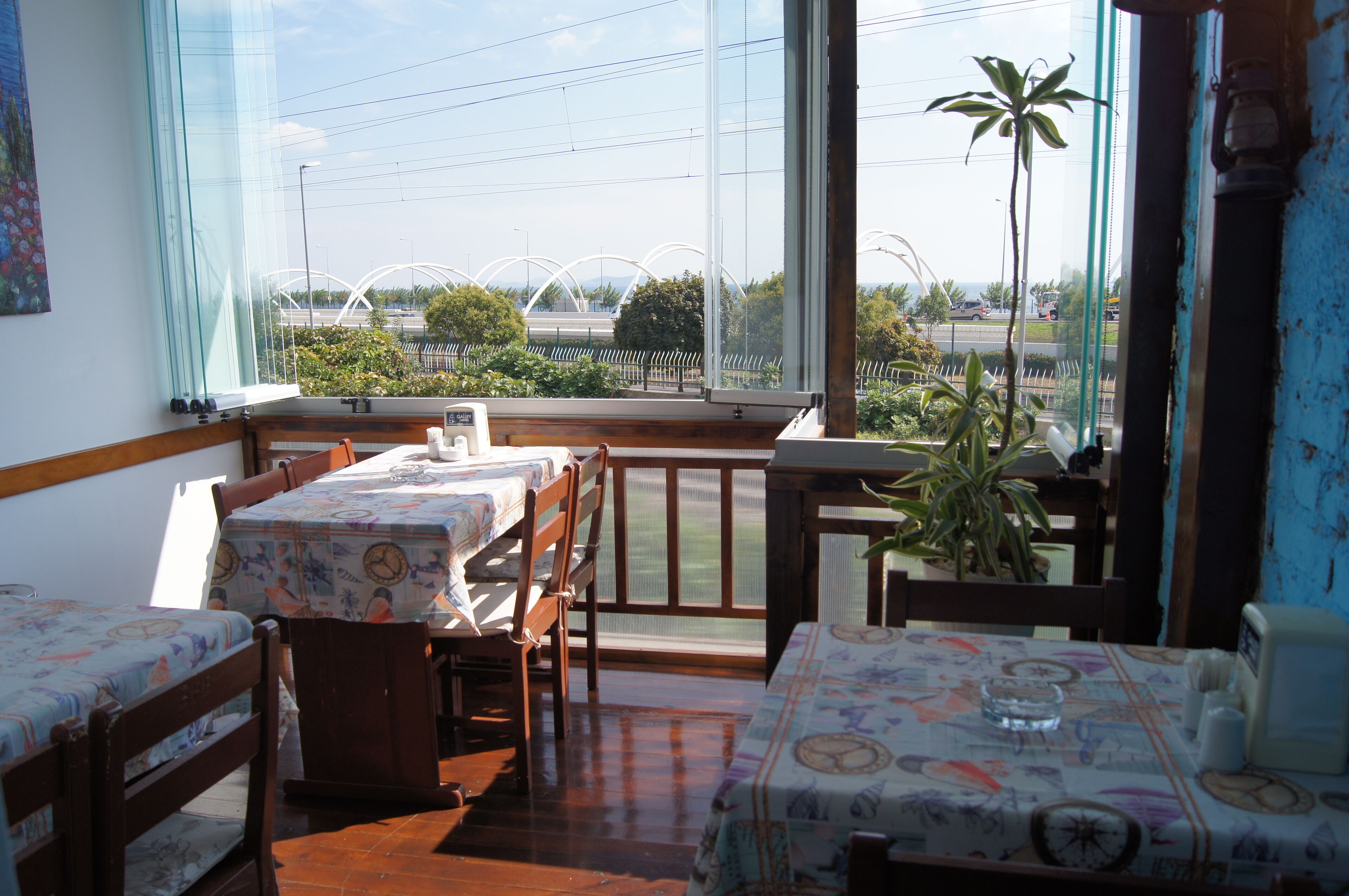 A room with two wooden beds, a dining table, and a large window offering a view of a road and greenery.