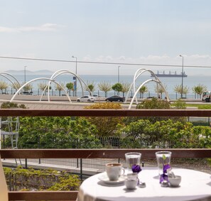 A table with a cup and saucer, a glass, and a small bowl, set against a backdrop of a coastal view with a bridge and ships in the distance. - Galley Hotel (Istanbul)