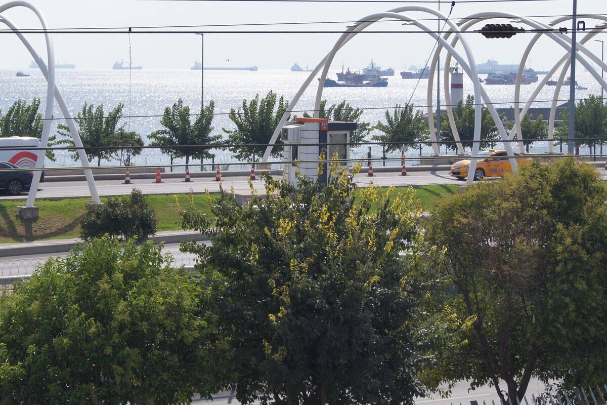 A coastal road with a bridge, vehicles, and ships in the background.
