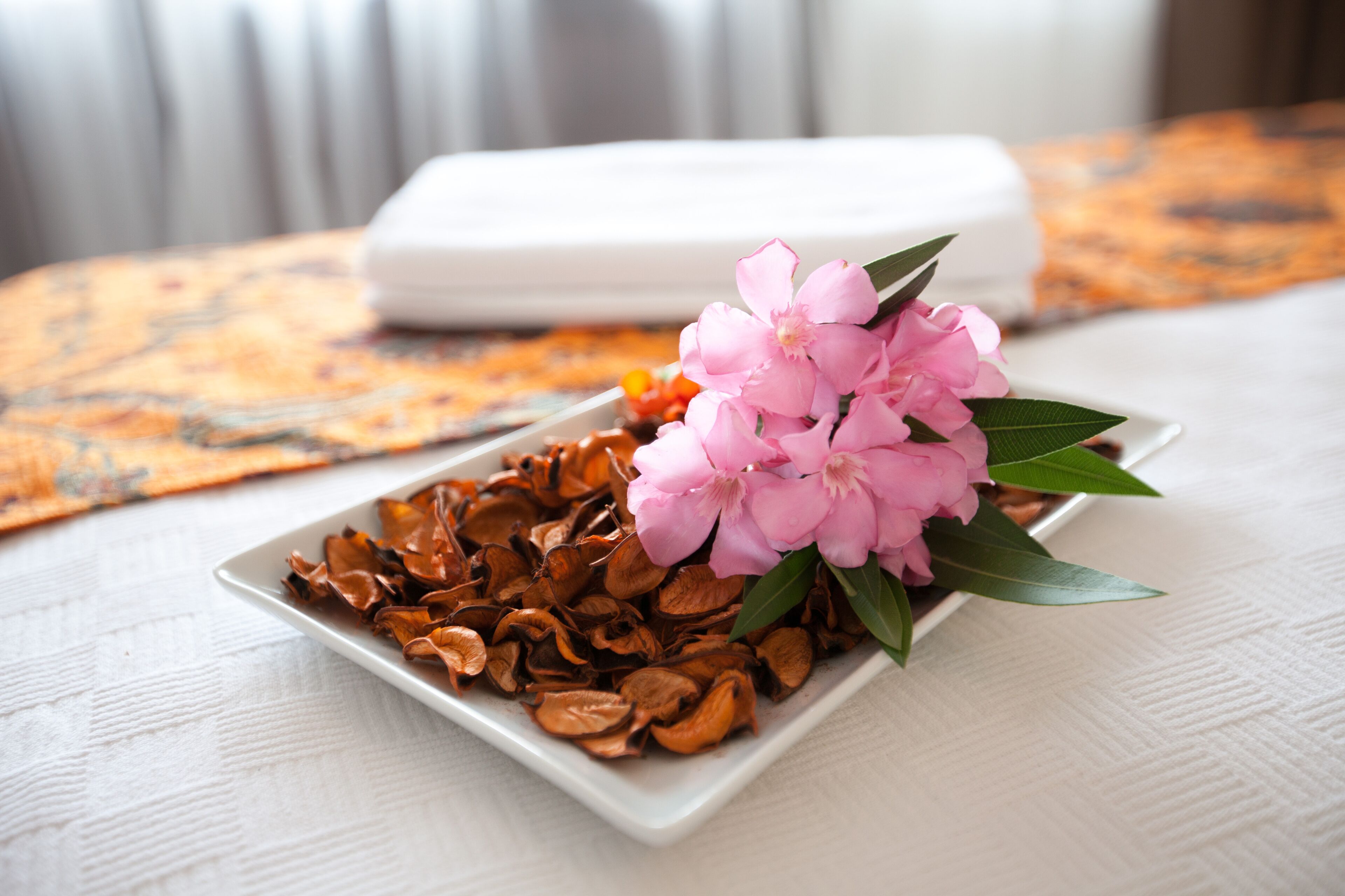 Un plato blanco con flores secas y hojas verdes sobre un mantel blanco texturizado.