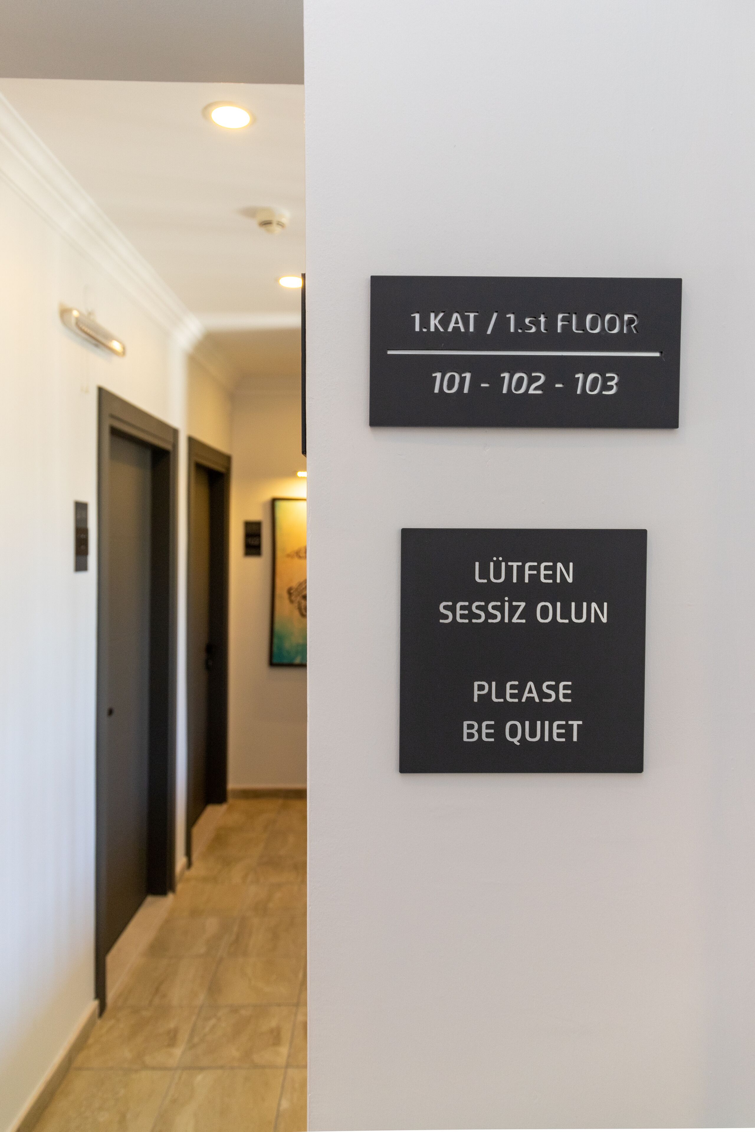 Un couloir avec une signalétique indiquant les numéros de chambre 101 à 103, situés au premier étage.