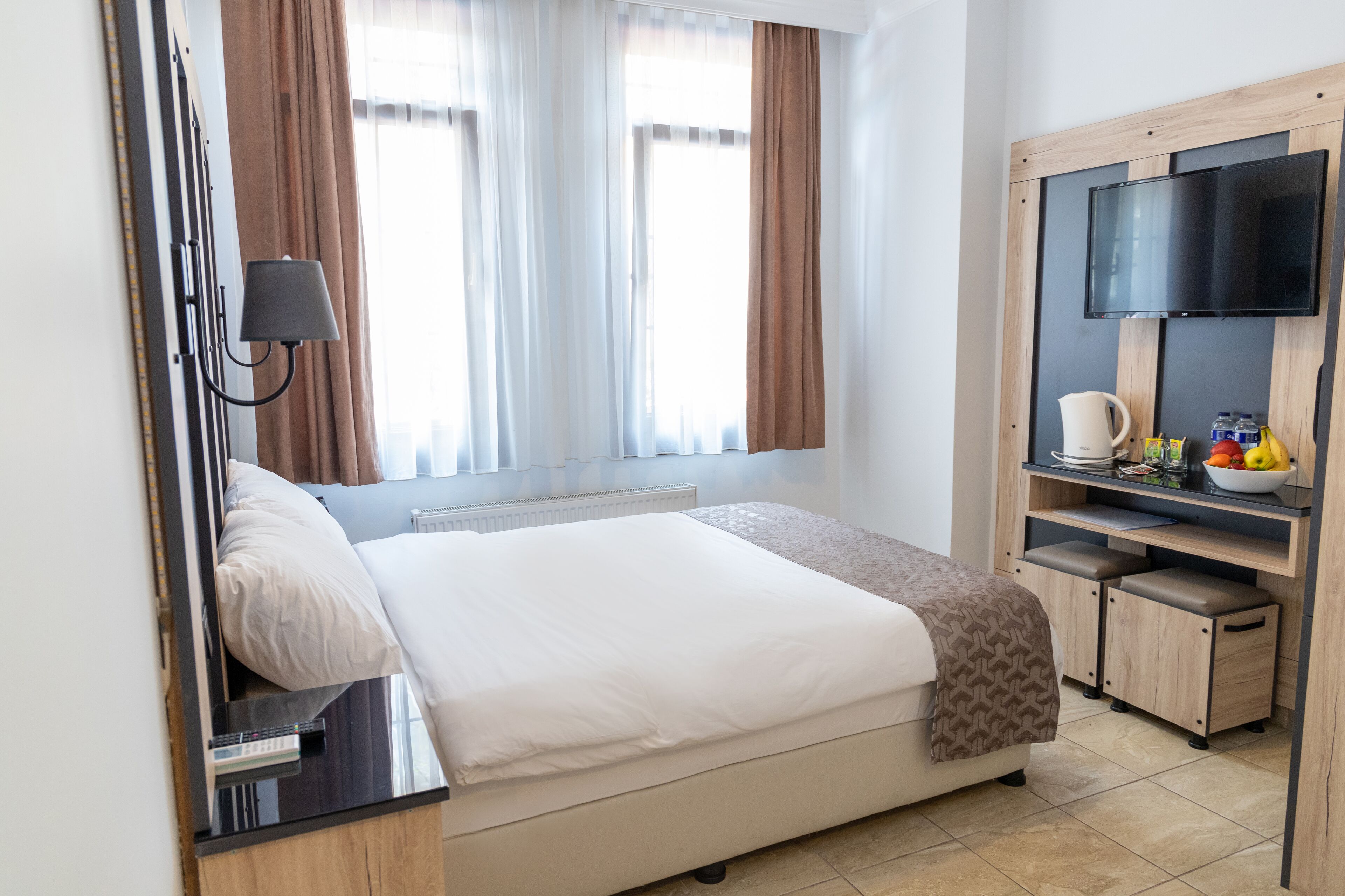 A hotel room with a bed, a TV, a desk with a lamp, a coffee maker, and a fruit bowl.