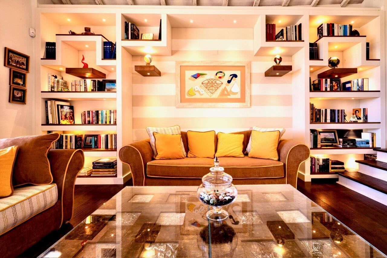 A living room with a sofa, a glass coffee table, and bookshelves filled with books and decorative items.
