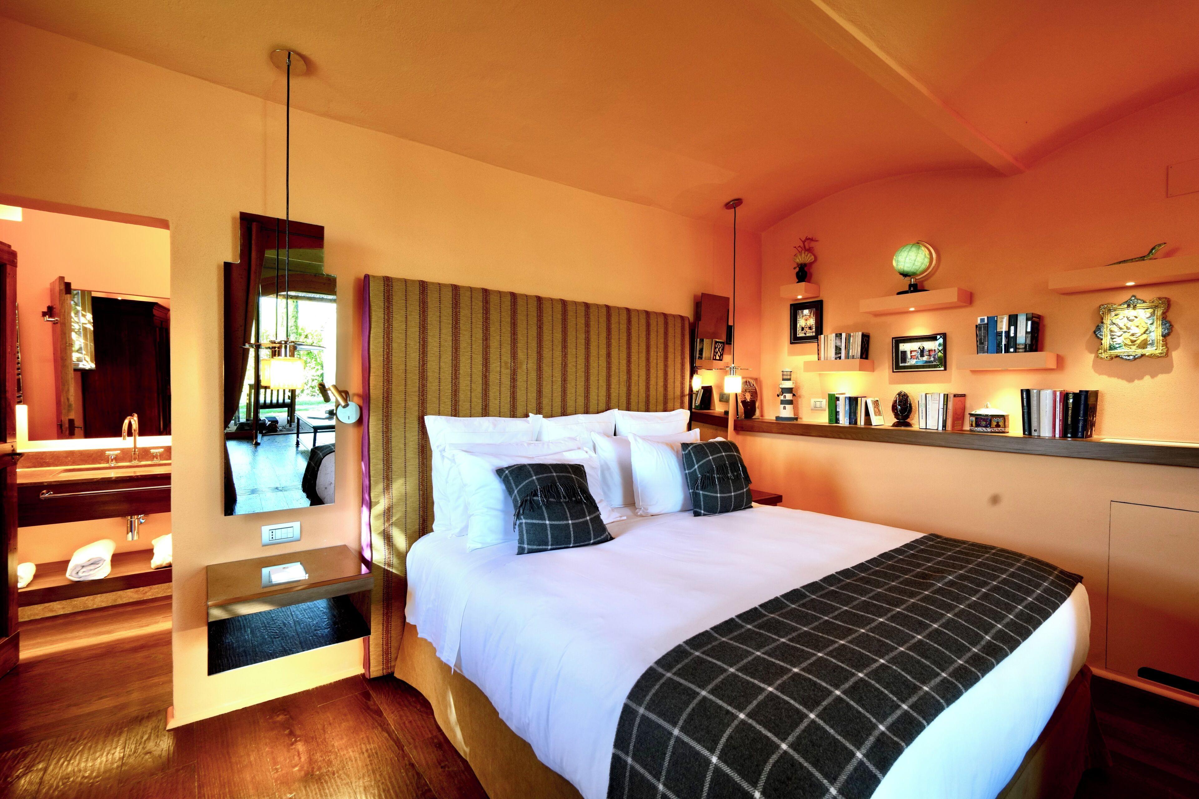 Une chambre d’hôtel avec un grand lit, un miroir, une table de chevet et un petit bureau avec une lampe.