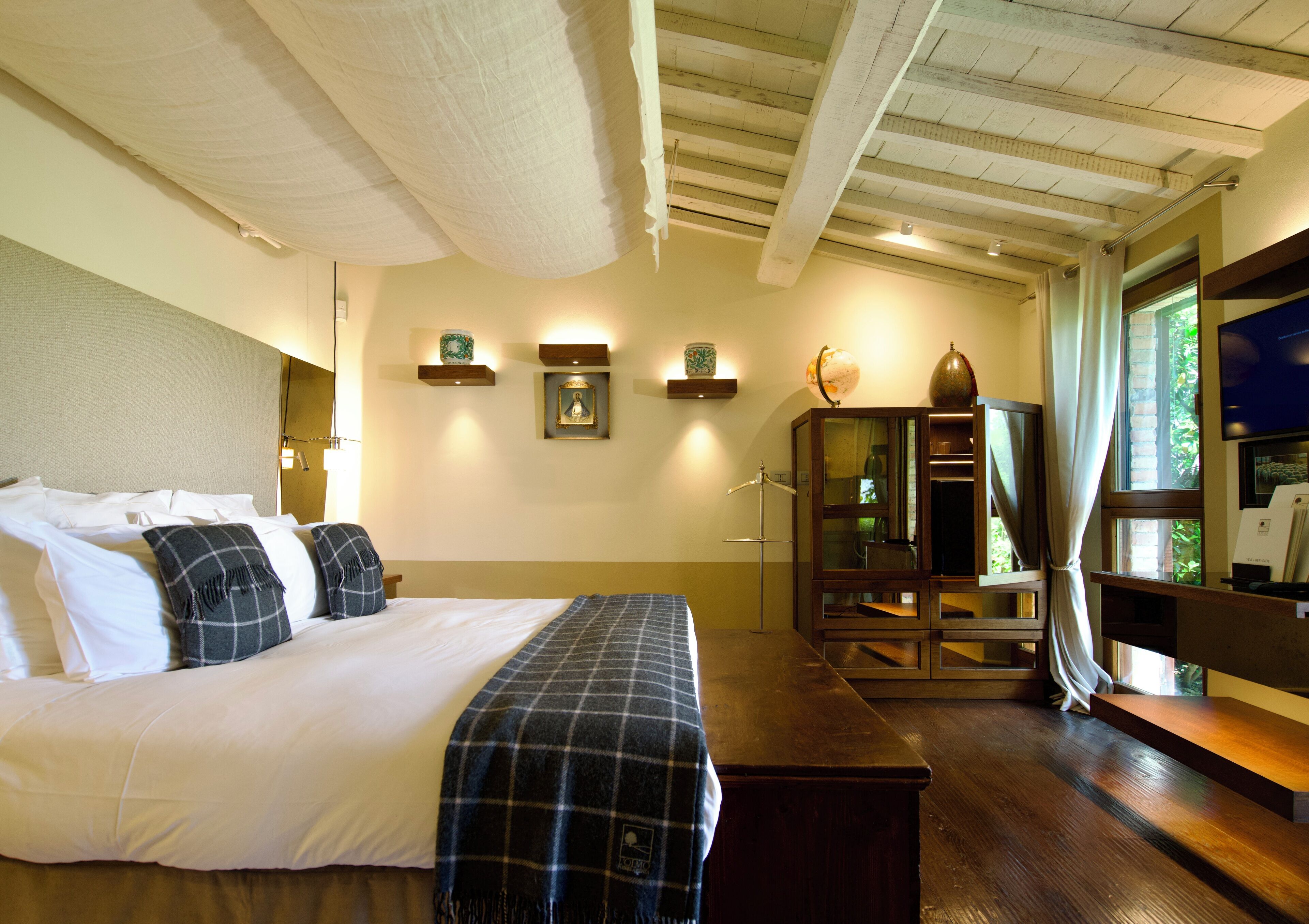 Une chambre d’hôtel avec un grand lit, un banc en bois, une télévision et un meuble avec des portes en verre.