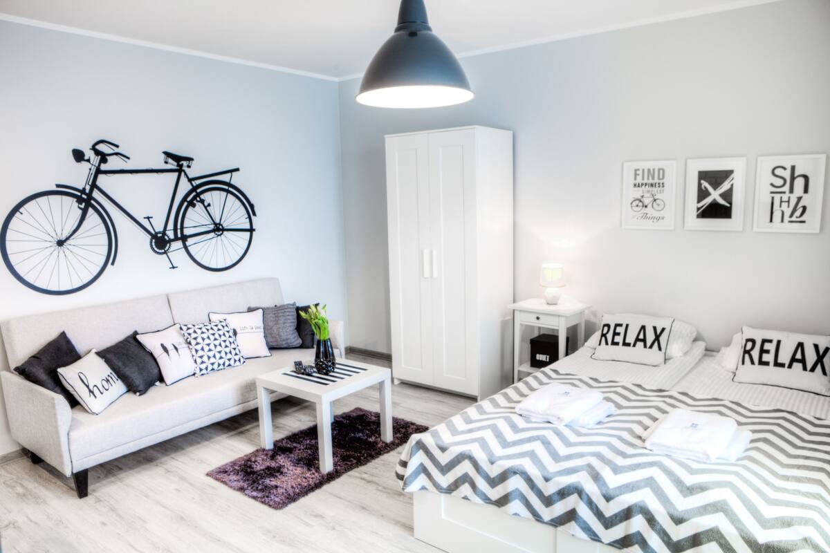 Un dormitorio moderno con una cama, un armario blanco, un sofá blanco, una mesita de centro y una obra de arte con una bicicleta colgada en la pared.